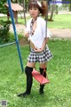 A woman in a school uniform is sitting on a swing.