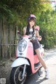 A woman sitting on a pink and white scooter.