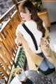 a woman sitting on a balcony wearing a beige coat