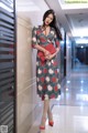 A woman in a floral dress leaning against a wall.