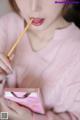 A woman in a pink sweater holding a stick in her mouth.