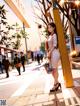 A woman in a white dress is standing on a sidewalk.