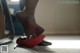 A woman's foot with a pair of red shoes on the floor.