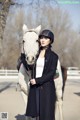 A woman standing next to a white horse wearing a helmet.