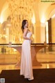 A woman in a long dress standing in front of a chandelier.