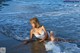 A woman in a white bikini laying in the ocean.