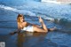 A woman in a white bathing suit laying on the beach.