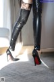 A woman wearing black leather thigh high boots and stockings.