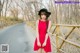 A woman in a red dress and black hat standing on a bridge.