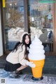 A woman kneeling down next to an ice cream cone.