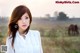 A woman standing in a field with a horse in the background.