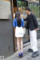 A woman in a blue shirt and white skirt is walking down the street.