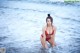 A woman in a red bikini sitting in the ocean.