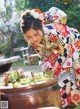 A woman in a kimono preparing food in a large pot.