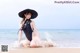 A woman in a black bathing suit and hat sitting on the beach.