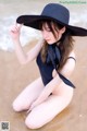 A woman in a black bathing suit and hat sitting on the beach.