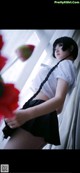 A woman in a white shirt and black skirt holding a red flower.