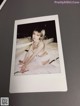 A polaroid photo of a woman sitting on a bed.