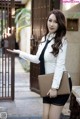 A woman in a white shirt and black skirt holding a brown purse.