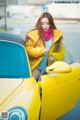 A woman in a yellow jacket leaning out the window of a yellow car.