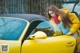 A woman leaning on the door of a yellow sports car.