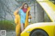 A woman standing next to a yellow car with the hood open.