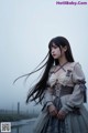 A woman with long black hair standing next to a body of water.