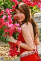 A woman in a red dress standing in front of a bush of flowers.