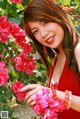 A woman in a red dress standing in front of a bush of flowers.