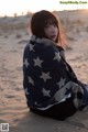 A woman wrapped in a blanket sitting in the sand.