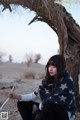 A woman sitting under a tree in the desert.