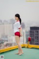 A woman in a white shirt and red shorts standing on top of a building.