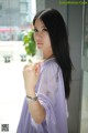 A woman in a purple dress standing by a window.