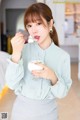 A woman holding a glass of milk and a spoon.