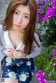 A young woman posing in front of purple flowers.