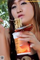 A woman eating a bowl of noodles with a fork.