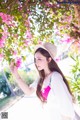 A woman in a white dress and hat holding a pink flower.