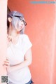 A woman wearing glasses leaning against a pink wall.