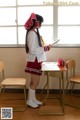 A woman in a school uniform standing in front of a desk.