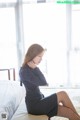 A woman in a black dress sitting on a bed.