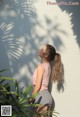 A woman standing in front of a white wall with a palm tree.