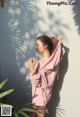 A woman in a pink shirt leaning against a wall.