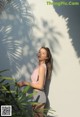 A woman leaning against a wall next to a plant.