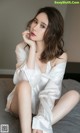 A woman sitting on top of a bed wearing a white shirt.