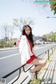 A woman in a red dress and white jacket sitting on a railing.