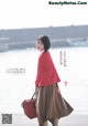 A woman in a red jacket and brown skirt holding a red bag.