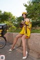 A woman in a yellow raincoat and helmet sitting on a wall.