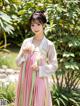 A woman in a pink and green hanbok standing in a garden.