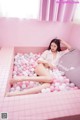 A woman laying in a pink bathtub filled with pink and white balloons.