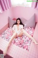 A woman sitting in a pink bathtub filled with pink and white balls.